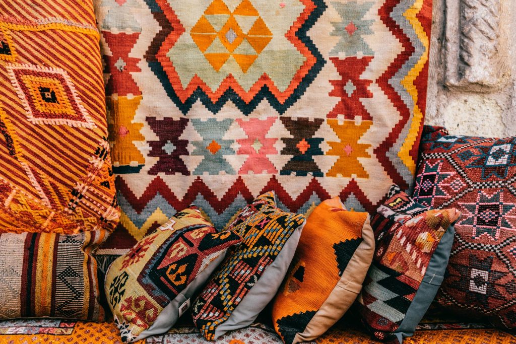 Colorful pillows with patterns placed on couch near abundance of ornamental oriental carpets on bazaar in old city on street